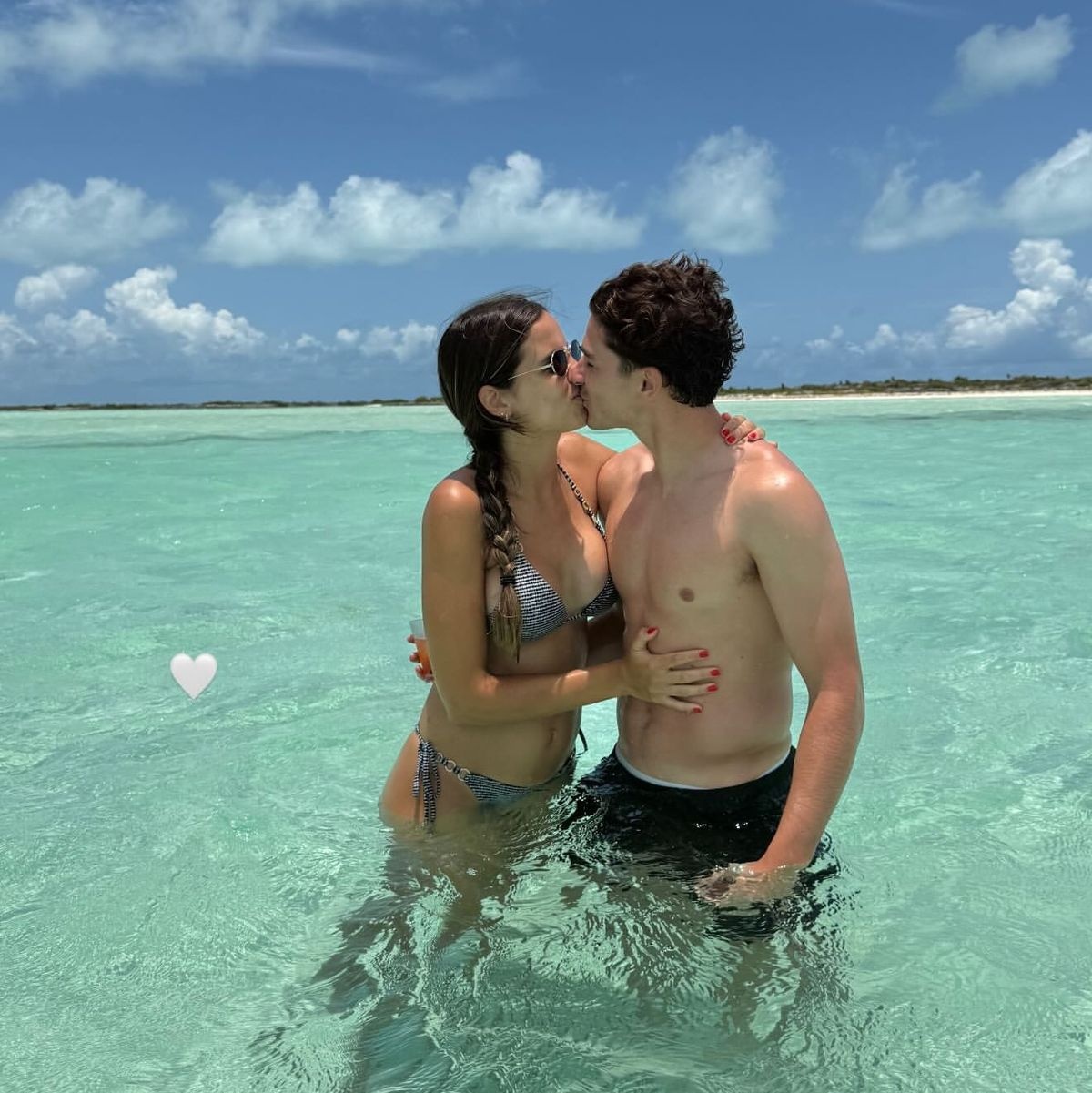 Couple kissing in clear turquoise ocean water under blue sky representing private tropical escape